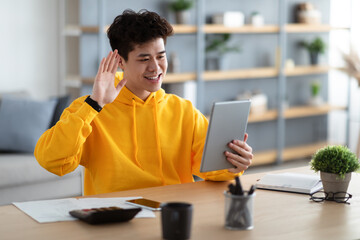 Wall Mural - Smiling asian man holding digital tablet waving hand