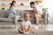 © Prostock-studio - Domestic Quarrels. Cute infant baby boy sitting alone separately from arguing parents