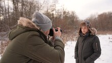 Closeup View Slow Motion 4k Stock Video Footage Of Handsome Bearded Professional Photographer Taking Cute Winter Pictures Of European Smiling Happy Teenage Kid At Snowy Nature Background. Focus On Man