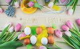 Happy easter karta, na drewnianym stole ułożone jajka, tulipany, żółte piórka, dekoracja wielkanocna.