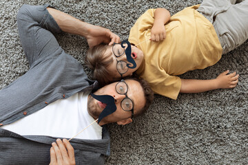 Movember concept. Funny surprised father and and little son wearing eyeglasses holding moustache photo props, top view