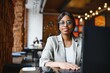 © Serhii - Head shot portrait of happy smiling African American woman sitting at table in cafe, looking at camera, excited female posing, working at computer, doing homework, preparing report in coffee house