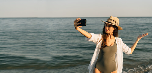 woman in white clothes makes a video call using an application on a mobile phone at sunrise over a sea beach outdoors on a summer day sunset in the evening while on vacation on a tropical beach.