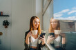 © ADDICTIVE STOCK - Cheerful lady with cup of coffee browsing smartphone near window