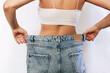 © Марина Демешко - Cropped shot of a young slender tanned woman standing with her back dressed in wide jeans and white top demonstrates successful weight loss isolated on a white background. Diet and wellness concept