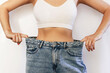 © Марина Демешко - Cropped shot of a young slender woman dressed in wide jeans and white top demonstrates successful weight loss isolated on a white background. Diet and wellness concept