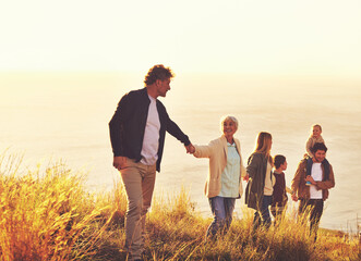 Say yes to adventure. A multi-generational family walking up a grassy hill together at sunset with the ocean in the background.