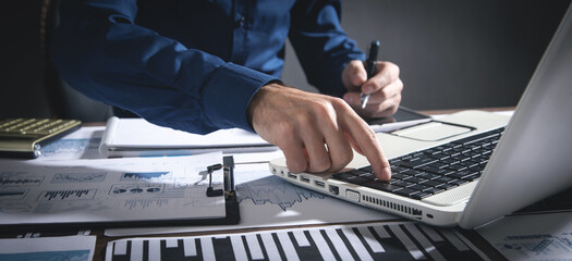 Businessman using laptop computer and working in financial graphs.