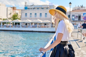 Young teenage female in hat on city sea embankment, copy space.