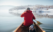 Rear View Of Man In Red Jacket Paddling Canoe On Lake Winter Ride