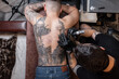 © alones - Tattoo artist man with black gloves draws a knight tattoo on the guy's back in the studio, top view. Tattoo artist's workflow