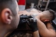 © alones - Young man tattoo artist with a tattoo machine professionally filling a tattoo in a studio. Creative working process