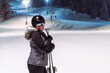 A woman enjoys her night skiing session.Illuminated ski slopes are in the background