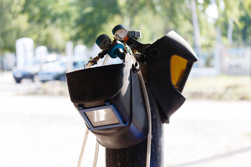 Welding equipment, helmet hanging on a gas cylinder, two welder masks. there are no people