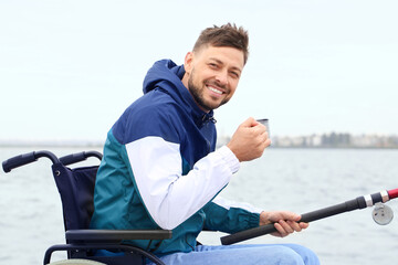 Canvas Print - Man in wheelchair drinking tea while fishing on river