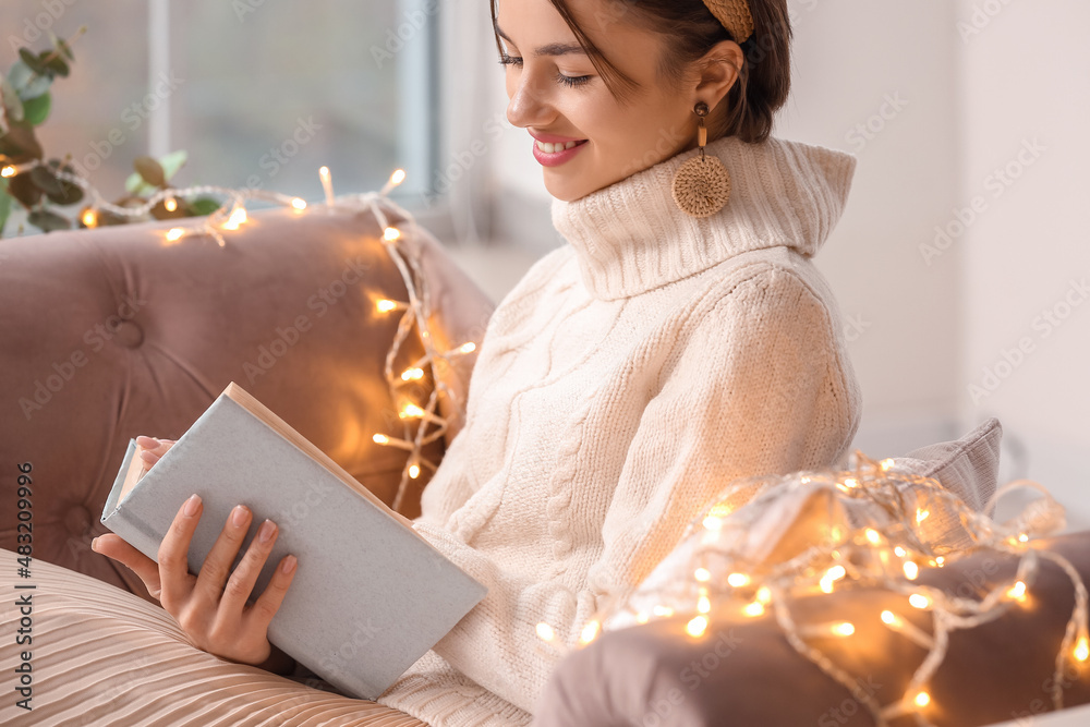 Beautiful young woman reading book on sofa at home