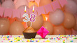 Decorations with balloons and a happy birthday candle with the number 38 for a woman. Happy birthday greetings in pink flowers for thirty-eight years for a girl, copy space. Muffin with a burning cand