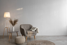 Retro armchair with plaid, luminous lamp, dry plants in vase on table, ottoman and round carpet