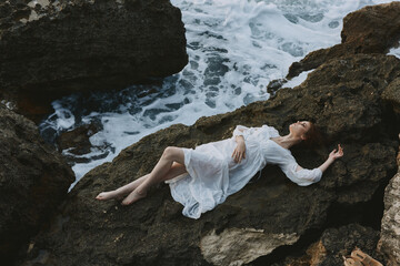 Poster - woman in long white dress wet hair lying on a rocky cliff vacation concept