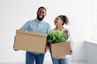 © Prostock-studio - Happy young african american woman and guy carry cardboard boxes with belongings and plant in empty room
