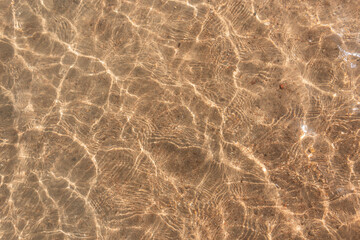 Beautiful clear water with light reflections and waves over yellow sandy beach, top view. Abstract water texture. Summer vacation on the red sea