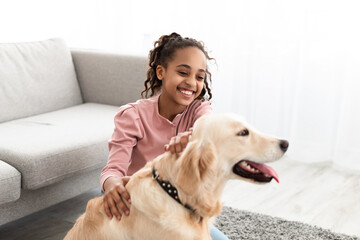 Wall Mural - Young black girl playing with dog in living room