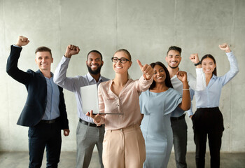 Young Businesswoman With Laptop Gesturing Thumb Up While Posing With Joyful Colleagues