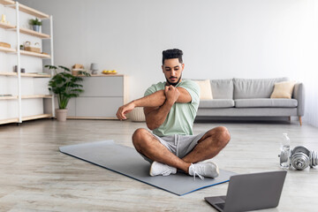 Wall Mural - Athletic young Arab man doing yoga in front of laptop during home workout, copy space