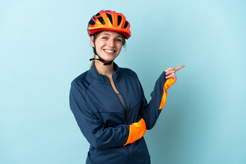 Wall Mural - Young cyclist woman isolated on blue background pointing finger to the side