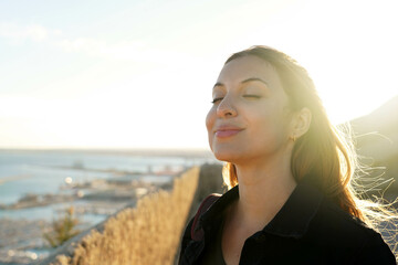 Beautiful young woman with closed eyes breathing with wind on her face relaxing enjoying sun at sunset. Beauty sunshine girl side profile portrait. Positive emotion life success mind peace concept.