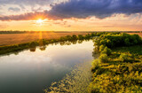 Fototapeta Las - Amazing view at scenic landscape on a beautiful river and colorful sunset with reflection on water surface and glow on a background, spring season landscape