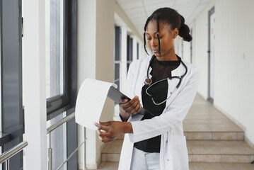 Poster - Portrait Of Smiling Female Doctor Wearing Scrubs In Hospital Corridor Holding Digital Tablet