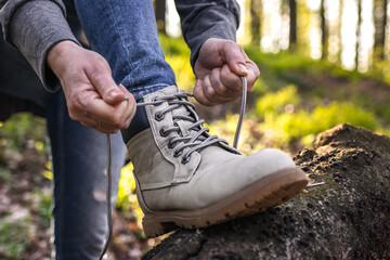 Wall Mural - woman tying shoelace on her hiking boot. tourist is getting ready for hike at forest trekking trail.