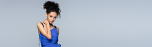 Curly African American Model In Bright Blue Dress Looking At Camera While Posing Isolated On Grey, Banner.