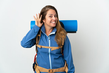 Wall Mural - Middle age mountaineer woman with a big backpack over isolated background listening to something by putting hand on the ear