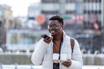 Young African American entrepreneur business man holding coffee in cardboard cup and talking on phone