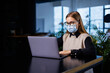 © DSMT - A beautiful smart businesswoman in a large company holds an online meeting with business partners in a protective mask during the coronavirus, she sits at a table at a workplace with a laptop