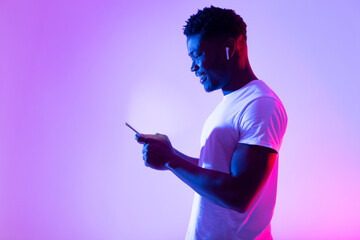 Poster - Online life concept. Millennial black guy using mobile phone, checking web or social media in neon light, copy space