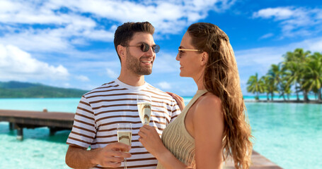 Poster - leisure, travel and tourism concept - happy couple in sunglasses drinking champagne over tropical beach background in french polynesia