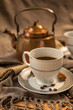 Two cups of coffee, a copper teapot in the background, shades of brown and gray, fabric in shades of gray