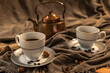 Two cups of coffee, a copper teapot in the background, shades of brown and gray, fabric in shades of gray