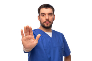 Wall Mural - healthcare, profession and medicine concept - male doctor in blue uniform showing stop gesture over white background