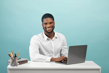 Wall Mural - Entrepreneurship and own business. Happy black businessman sitting at laptop over blue background