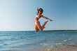 © Syda Productions - people, summer and swimwear concept - happy smiling young woman in bikini swimsuit jumping on beach