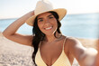 © Syda Productions - people, summer and swimwear concept - happy smiling young woman in bikini swimsuit and straw hat taking selfie on beach