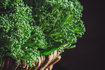 fresh bimi vegetable on a dark table. closeup of raw baby broccoli in a basket.