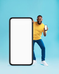 Poster - Handsome black guy standing near giant cellphone with blank screen, showing mobile device on blue background, mockup
