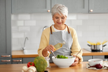 Sticker - healthy eating, food cooking and culinary concept - happy smiling senior woman with olive oil making vegetable salad on kitchen at home