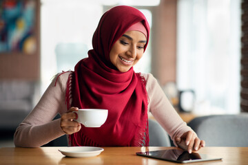 Wall Mural - Woman in hijab chilling at cafe alone, using digital tablet