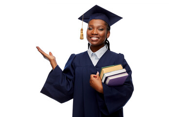 Wall Mural - education, graduation and people concept - happy graduate student woman in mortarboard and bachelor gown with books showing something imaginary over white background